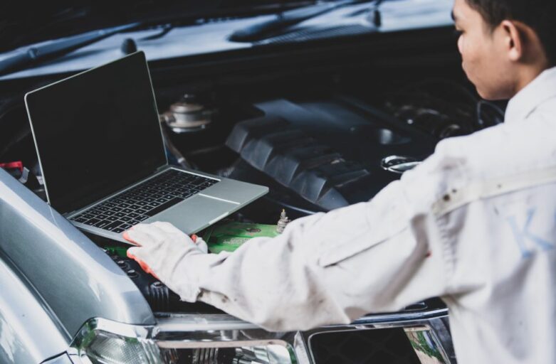 A mechanic uses a laptop computer to diagnose a car engine with the hood open.