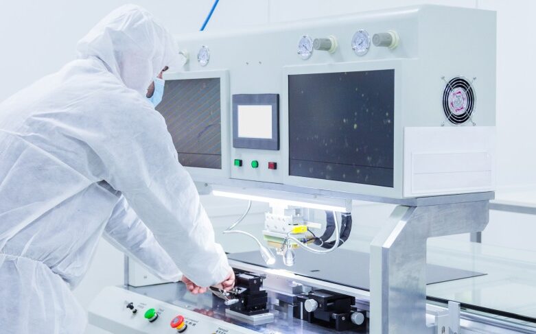 A person in protective clothing operates a machine with screens and buttons in a clean laboratory, ensuring AMT Precision Parts for high accuracy medical and industrial applications are manufactured to exact standards.