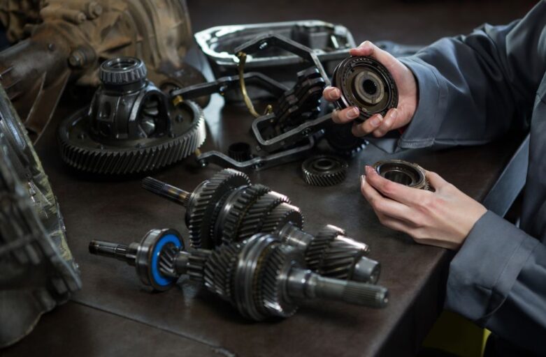 Person holding gears at a workbench with various gearbox components and mechanical parts laid out in front of them, inspecting for common signs you need gearbox repair.